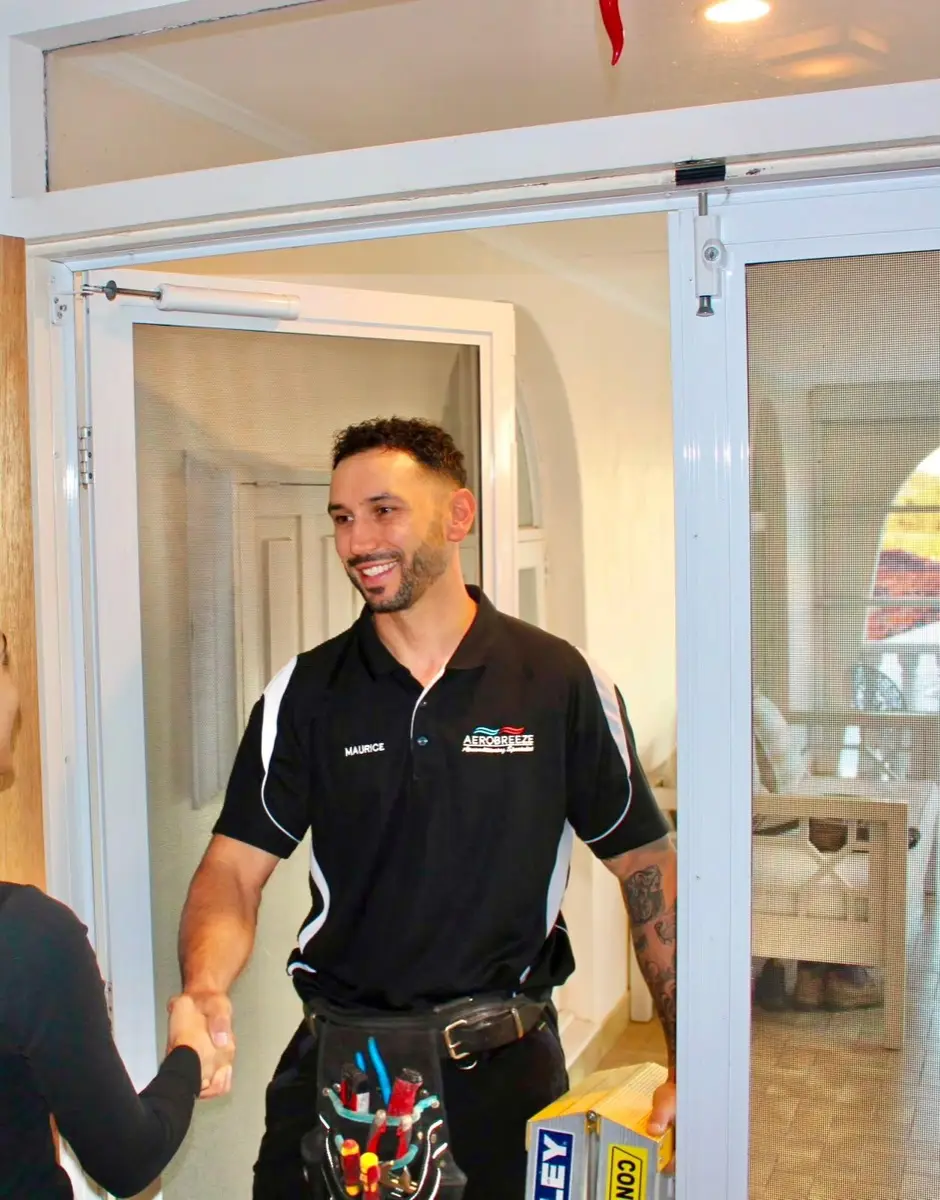Maurice, owner of Aerobreeze, shaking hands with a customer at their front door, tool belt on and ladder in hand