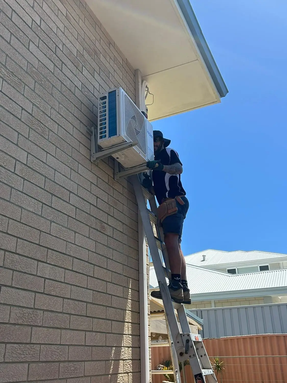 Aerobreeze technician on a ladder installing a wall split system on a brick wall